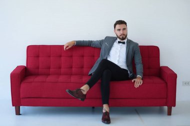 Genç bir adam oturuyor ve kırmızı kanepede bir akıllı telefon kullanma.