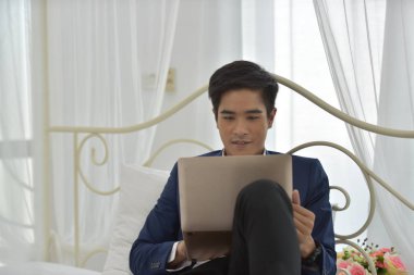 Yatakta dizüstü bilgisayar kullanan Asyalı bir adam