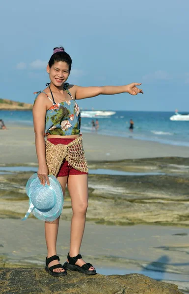 The beautiful girl is sending a sweet smile and a cheerful gesture with the view of the sandy beach,