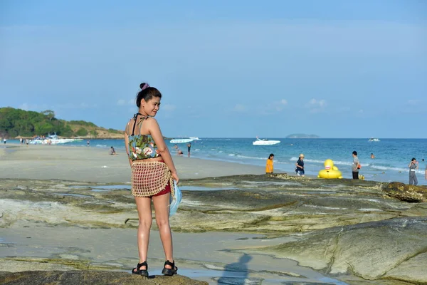 The beautiful girl is sending a sweet smile and a cheerful gesture with the sandy beach