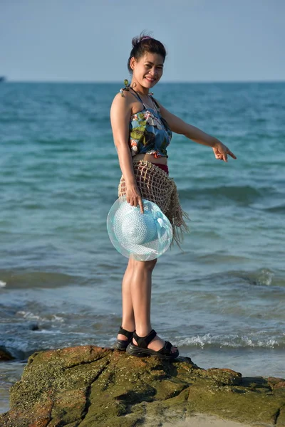 The beautiful girl is sending a sweet smile and a cheerful gesture with the view of the sandy beach,