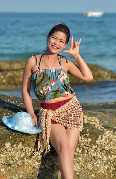 The beautiful girl is sending a sweet smile and a cheerful gesture with the sandy beach