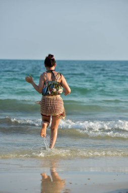 Güzel kız kumlu plaj manzarası ile tatlı bir gülümseme ve neşeli bir jest gönderiyor,