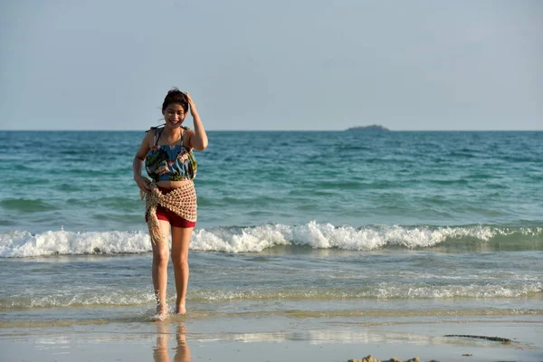 The beautiful girl is sending a sweet smile and a cheerful gesture with the view of the sandy beach,