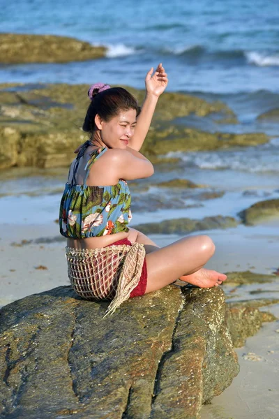 The beautiful girl is sending a sweet smile and a cheerful gesture with the view of the sandy beach, the blue sea, the waves and the sky on a bright day.