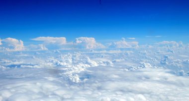 Kabarık bulutlu mavi gökyüzünde uçak penceresinden görünüm 