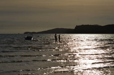 İnsanlar gün doğumunda deniz kıyısında dinleniyorlar.