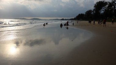 İnsanlar okyanus kıyısında gün batımının keyfini çıkarıyor.