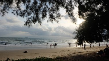 İnsanlar okyanus kıyısında gün batımının keyfini çıkarıyor.