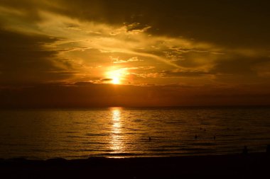 Güzel plaj manzarasında gün doğumu birçok insan gün batımından önce denizde oynamak için geliyor.plajda gün doğumu silueti.