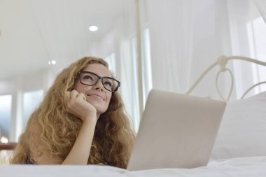 yatakta yatarken dizüstü bilgisayar üzerinde çalışan güzel sarışın kadın 