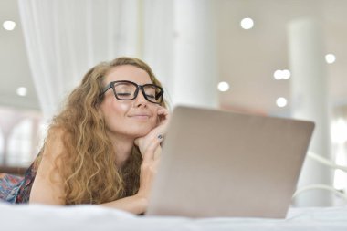 yatakta yatarken dizüstü bilgisayar üzerinde çalışan güzel sarışın kadın 