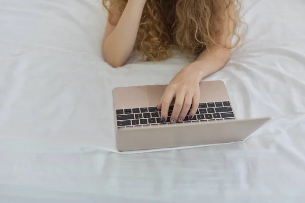 beautiful blonde woman working on laptop while lying in bed