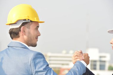Sert şapkalı işadamları birlikte çalışıyor, şehrin arka planında el sıkışıyorlar..