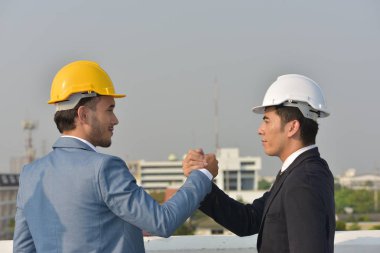 Sert şapkalı işadamları birlikte çalışıyor, şehrin arka planında el sıkışıyorlar..
