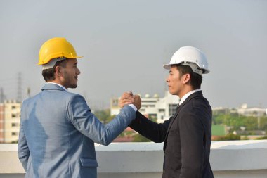 Sert şapkalı işadamları birlikte çalışıyor, şehrin arka planında el sıkışıyorlar..