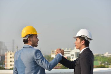 Sert şapkalı işadamları birlikte çalışıyor, şehrin arka planında el sıkışıyorlar..