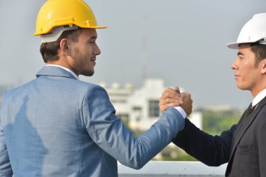 Sert şapkalı işadamları birlikte çalışıyor, şehrin arka planında el sıkışıyorlar..