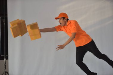 Turuncu servis üniformalı genç Asyalı işçi paketleri bırakıyor.