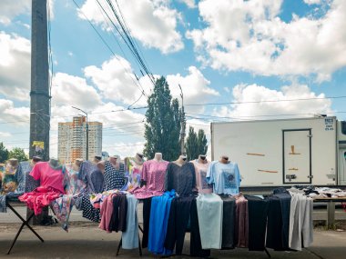 Kyiv, Ukrayna, 17 Ağustos 2025, Kyiv 'deki sokak pazarı. Mankenler üzerinde renkli giysiler sergileniyor. Yüksek binalar, ağaçlar ve parlak bulutlu bir yaz gökyüzü.