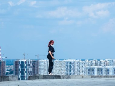 Kyiv, Ukraine 3d June,2025, Red haired woman in black clothing stands on elevated platform at Park of Eternal Glory in Kyiv, with panoramic view of modern residential buildings under blue sky