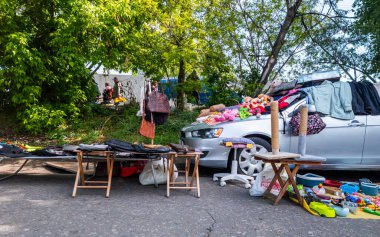 Kyiv, Ukraine 11th May,2025, Flea market stall with assorted secondhand items such as bags, stuffed toys, clothing, and household goods organized around a parked car on a tree lined sunny street