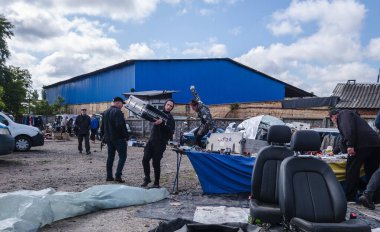 Kyiv, Ukraine 10th May,2025, Street market in Ukraine with people browsing second hand goods, electronics, and car parts on display under cloudy sky in front of blue warehouse building