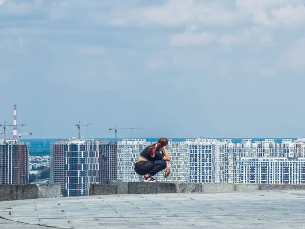 Kyiv, Ukraine 3d June,2025, Woman squats near a ledge at Park of Eternal Glory in Kyiv, gazing across modern skyscrapers and cranes, reflecting themes of solitude, urban expansion, and city life