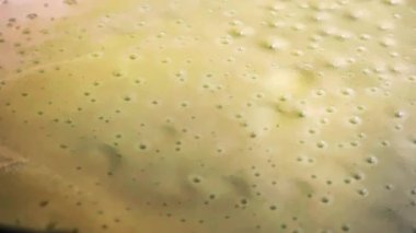 Macro view of a thick, creamy green vegetable soup simmering in a pot with bubbles gently rising and bursting, showing the cooking process of a healthy, homemade puree meal