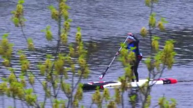 Athletic man in a wetsuit paddleboarding on a calm river, practicing balance and fitness amid autumn foliageoutdoor recreation, healthy lifestyle, and scenic leisure activity