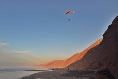 Yamaçparaşütü sahil üzerinde günbatımında uçar. Legzira kırmızı kayalık sahil beach, Fas.