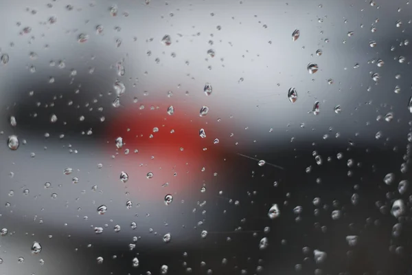 Yağmur damlaları penceresinde. Bulanık gri arka plan kırmızı ışık araba fener ile.
