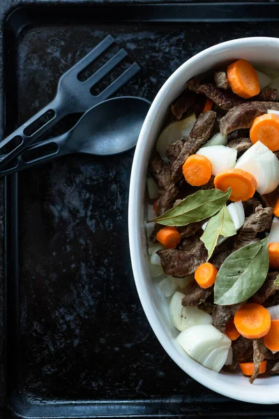 Siyah tepside et, havuç, soğan ve defne ile beyaz tabak. Yemek malzemeleri kaşığı ve çatalı. Üst Manzara. Boşluğu kopyala.