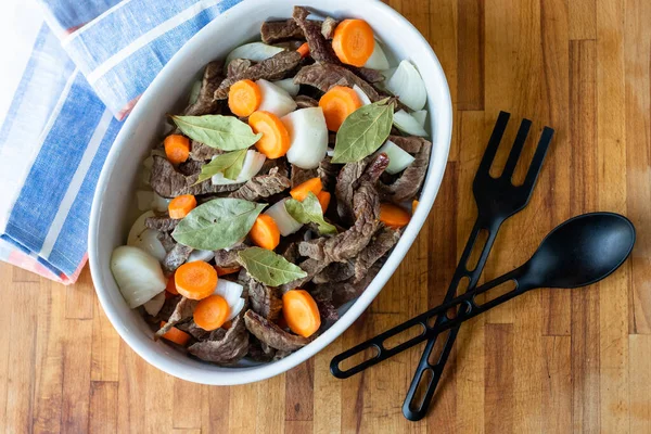 Tahta zemin üzerinde et, havuç, soğan ve defne ile beyaz tabak. Yemek malzemeleri kaşığı ve çatalı. Üst Manzara. Boşluğu kopyala.