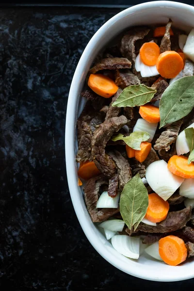 Siyah tepside et, havuç, soğan ve defne ile beyaz tabak. Üst Manzara. Boşluğu kopyala.