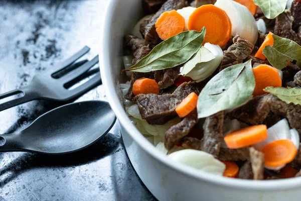 Siyah tepside et, havuç, soğan ve defne ile beyaz tabak. Yemek malzemeleri kaşığı ve çatalı..