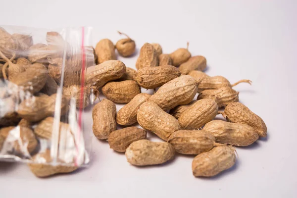 Amendoins ou amendoins que saem do saco plástico em fundo isolado — Fotografia de Stock