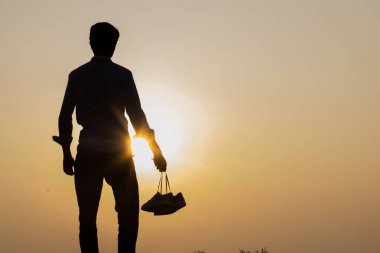 Gün batımında ayakta duran ve elinde ayakkabıları tutan çocuk. Yakın plan..