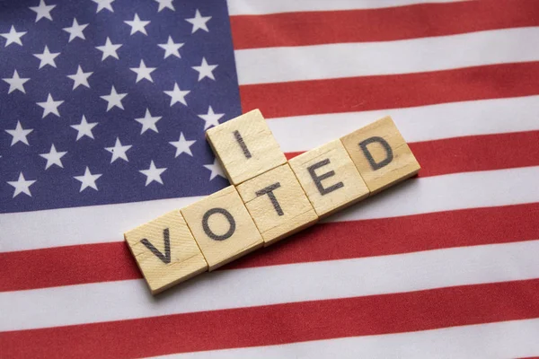 Maski, India 26, April 2019: I voted wooden block letters, US elections on American flag . — стоковое фото