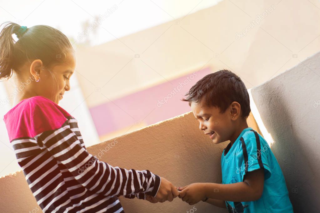 Two Indian kids brother and sister or siblings fighting for Mobile phone at outdoor.