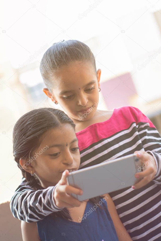 Two Indian kids watching mobile device at outdoor