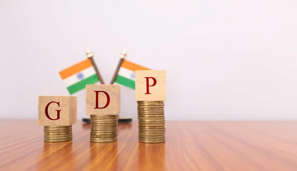 BNP eller bruttonationalprodukt i trä block bokstäver på mynt i stigande ordning med indiska flagga som bakgrund. — Stockfoto