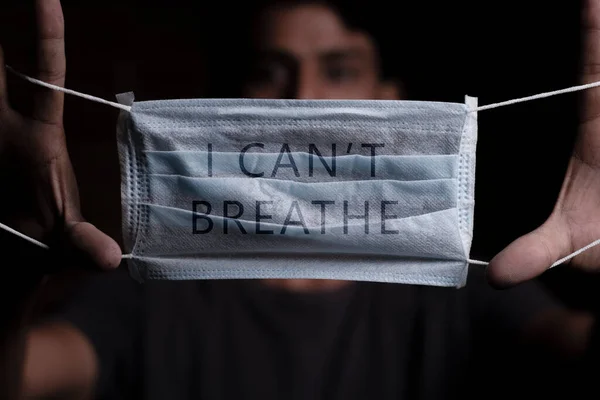 Young man holding medical mask with I Cant Breathe inscription on it. Cooncept of Protest about racial discrimination of Black People in U.S. America.