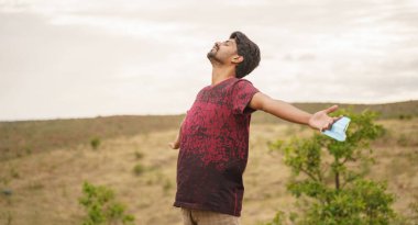 Genç adam, sağlık maskesini dağın tepesine çıkararak temiz hava alıyor. Maske saplantısından mutluluk kavramı ya da koronavirüs veya covid-19 karantinasından sonra ortaya çıkıyor..