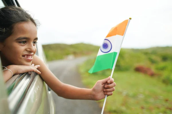 Happy Cheerful Young girl kid holding Indian flag out of in moving car window - Concept of patriotism and Independence or republic day celebration — Stock Photo, Image