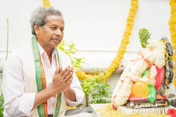 Starší muž nabízí Bhajan nebo chvalozpěv před lordem Ganesha Idol během Ganesha nebo vinayaka Chaturthi slavnostní ceremoniál doma. — Stock fotografie