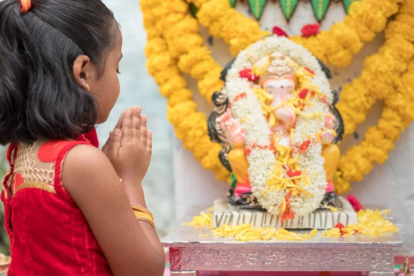 Niña rezando cerrando los ojos y doblando las manos delante del Señor Ganesha ídolo durante Ganesha o vinayaka ceremonia del festival Chaturthi en casa - concepto de celebraciones del festival religioso indio. —  Fotos de Stock