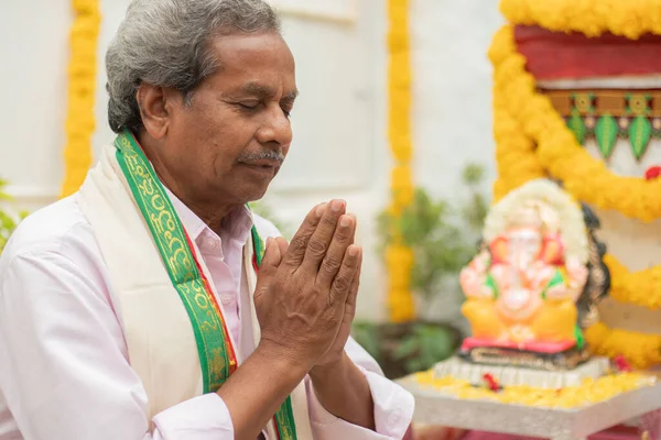 Starší muž nabízí modlitbu namaste gestem před lorda Ganesha Idol během Ganesha nebo vinayaka Chaturthi slavnostní ceremoniál doma. — Stock fotografie