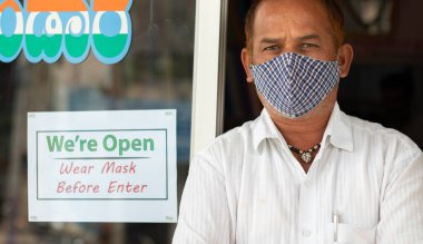 Tıbbi maskeli küçük işletme sahibi ile birlikte kapının önünde duruyoruz. Maske uyarı tahtası takıyoruz. Coronavirus ya da covid-19 sırasında yerel halkı destekleme kavramı.