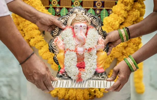 Senior Couples brought God ganesha idol and placing on decorated stage at home during vinayaka chaturthi festival - concept of Indian religious festival celebrations at home.